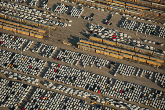 Aerial view of a vast vehicle storage lot filled with rows of parked cars and freight trains in an industrial area in Kansas City, Missouri, United States.