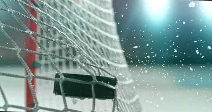 Extreme super slow motion close-up of an ice hockey puck striking the goal net at 1000 fps, with ice particles exploding on impact and a blurred winter stadium and rink in the background.