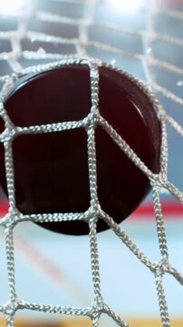 Super slow motion close-up of a hockey puck hitting the goal net as a player scores, captured at 1000 fps, with ice particles and a blurred hockey player on the rink in the background. Speed Ramp.
