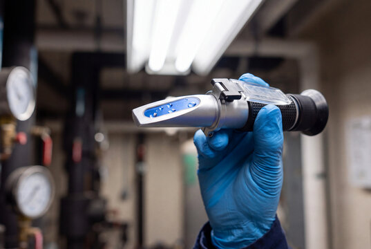 Lab Technician in Blue Gloves Checking Refractometer Reading in Industrial Facility