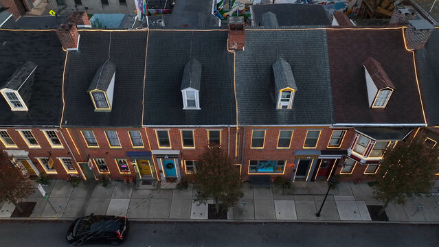 Aerial view of a row of historic brick houses with dormer windows and festive string lights along a quiet street in York, Pennsylvania, United States.