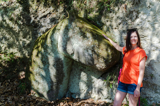 Woman touching ancient horse-shaped stone carving in volcanic rock during vacation in Italy.
