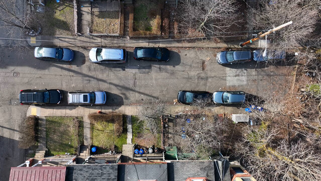 Aerial view of a residential street in the Oakland neighborhood with parked cars lining the road and bare trees during winter in Pittsburgh, Pennsylvania, United States.