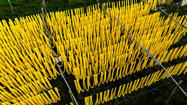 Aerial view of vibrant yellow fabric strips hanging to dry on bamboo frames over a green field in Narayanganj, Dhaka Division, Bangladesh.