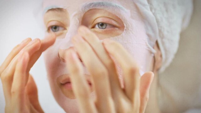 Woman's hands gently spread a cooling aloe vera mask across her skin in front of a bathroom mirror, embodying a dedicated at-home skincare ritual that hydrates, soothes and revitalizes her complexion