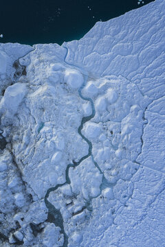 Aerial view of Ilulissat Icefjord with intricate meltwater channels carving through massive glacial ice formations and deep blue arctic waters in Ilulissat, Avannaata Municipalit, Greenland.