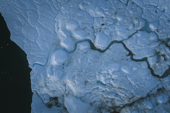 Aerial view of the Ilulissat Icefjord featuring intricate blue ice formations, deep meltwater channels, and textured glacial surfaces in Ilulissat, Avannaata Kommunia, Greenland.