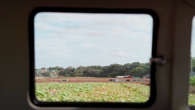 View from train window of passing rural green fields in countryside