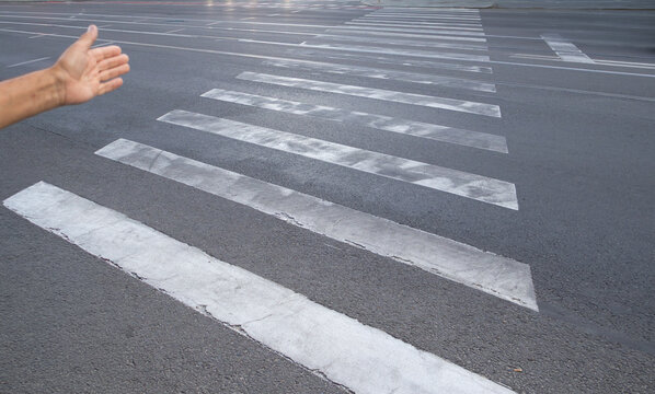 Outstretched hand gesturing toward a zebra crossing across an urban street with tram tracks