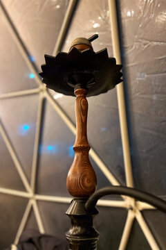 Wooden hookah stem standing in front of a geometric wall background in a dim indoor setting