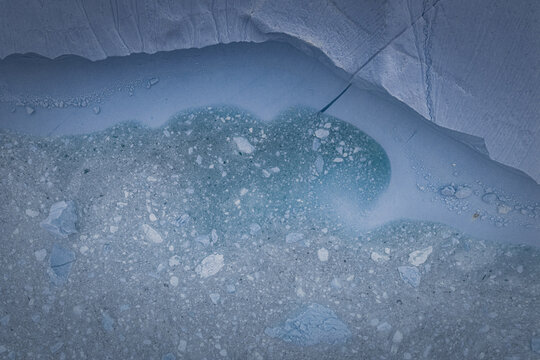 Aerial view of the Ilulissat Icefjord, showing intricate blue ice patterns, glacial meltwater, and floating ice fragments in the Arctic landscape in Ilulissat, Avannaata Kommunia, Greenland.