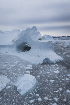Aerial view of a large iceberg with a natural arch floating in the icy waters of the Ilulissat Icefjord, surrounded by fragmented sea ice in Ilulissat, Avannaata Municipalit, Greenland.