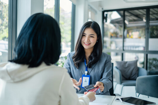 Smiling Asian banker offering credit card to client during financial consultation meeting in modern corporate office for professional banking service concept