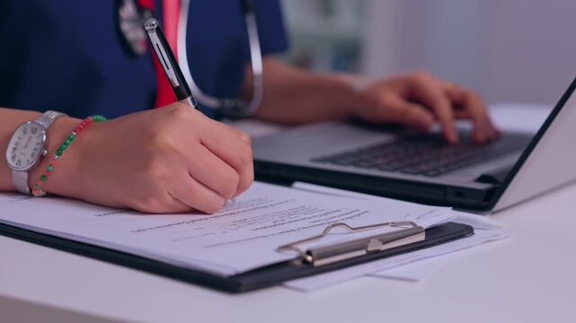 Doctor Writing Medical Notes Beside Laptop in Clinical Office with Stethoscope and Clipboard, Focused Healthcare Documentation, Patient Care, Professional Administration and Organized Paperwork