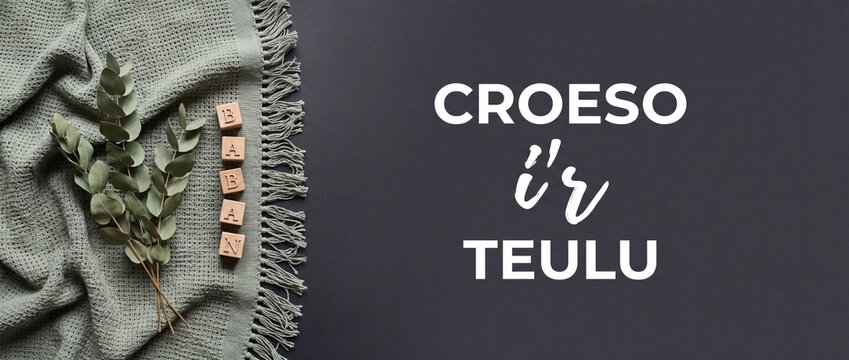Welsh baby announcement background banner with Croeso ir teulu text, featuring wooden blocks spelling baban and eucalyptus leaves on sage green woven blanket for modern minimal newborn arrival.