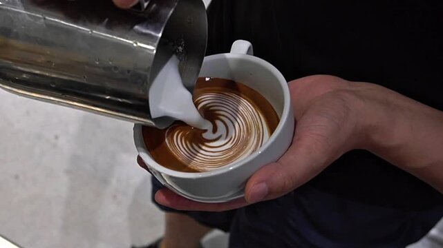Barista pouring steamed milk into espresso cup to create latte art
