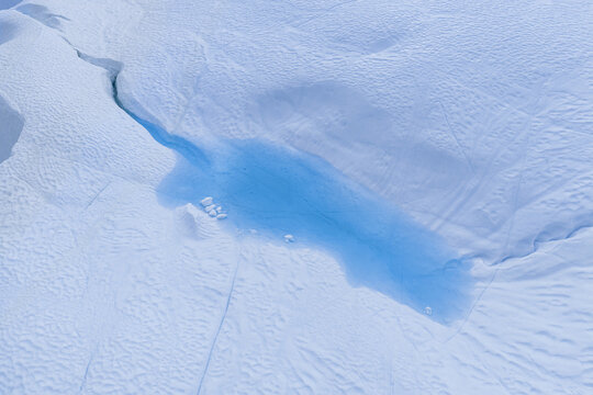 Aerial view of a bright blue meltwater pool within a deep glacial crevasse surrounded by vast white snow and ice fields in Ilulissat, Avannaata Municipalit, Greenland.