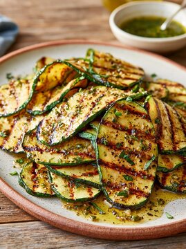 Plate of grilled zucchini slices on a wooden table. the slices are arranged in a circular pattern on the plate, with some overlapping each other.