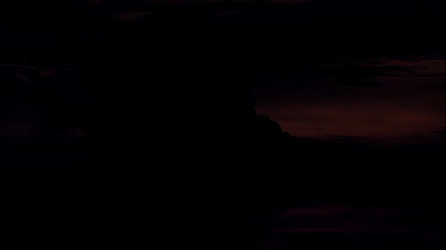 Sinking sharp sun disk descending rapidly next to towering dark silhouetted cumulus cloud structure while thin wispy fragments cross midway through glowing solar orbit.