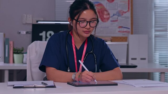 Female doctor writing medical notes desk clinical office, wearing glasses and stethoscope, focused physician professional documenting patient care with anatomy chart background for healthcare