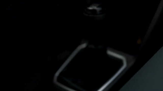Close up video frame of a driver's hand holding and shifting the manual transmission stick lever on the center console of an automobile. Modern car interior cockpit details with gear shift knob under