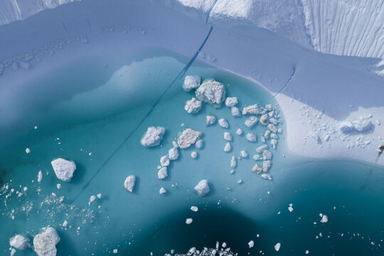 Aerial view of Ilulissat Icefjord featuring massive white icebergs floating in turquoise glacial water with intricate cracks in the surrounding ice shelf Ilulissat, Avannaata Kommunia, Greenland.