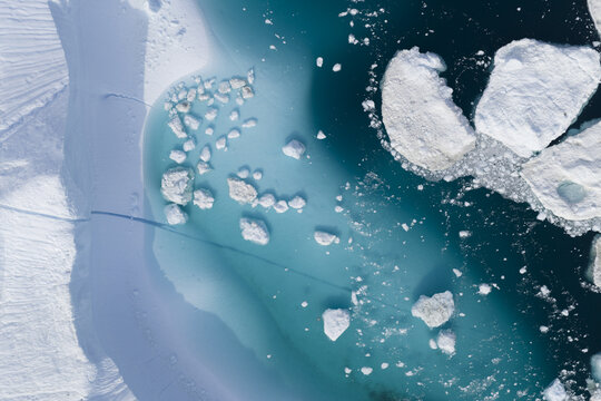 Aerial view of icebergs floating in the turquoise waters of the Ilulissat Icefjord, surrounded by snow-covered coastal ice in Ilulissat, Avannaata Municipalit, Greenland.