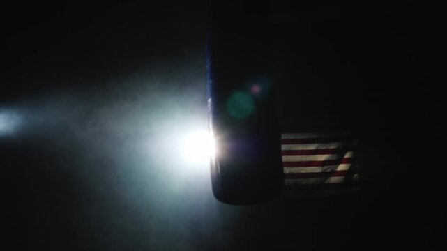 Boxing bag hanging in dark smoky gym illuminated by bright spotlight against American flag background slow motion footage showcasing dramatic atmosphere of training equipment for professional combat