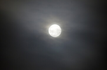 A beautiful close-up view of a bright full moon shining through dark cloudy sky at night. A dramatic natural background concept for astronomy, mysterious atmosphere, and midnight. © Andrew_Swarga