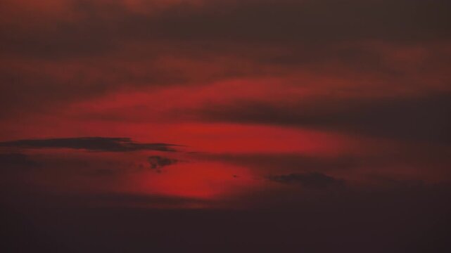 Distinct sun disk muted and attenuated by thick atmospheric veil, sunset telephoto time-lapse. Sun retains clear shape as it descends through dense layers of misty clouds, sky color changing to dark