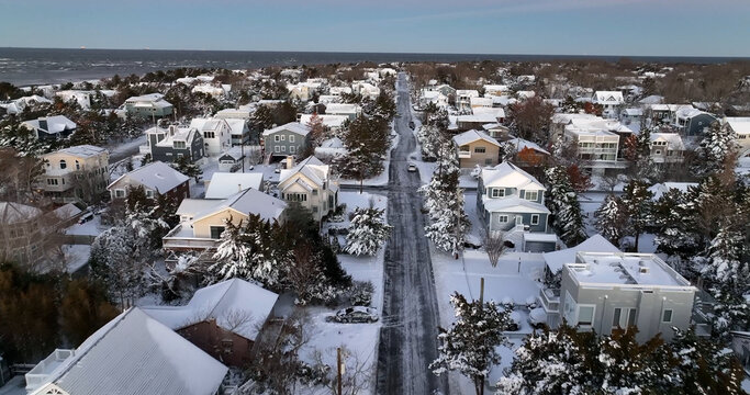 Aerial view of a snow-covered residential street lined with houses and trees leading toward the ocean in Cape May, New Jersey, United States.