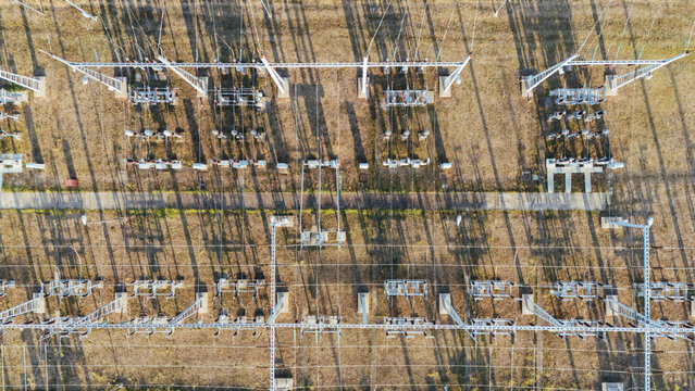 Aerial view of an electrical power substation with high-voltage equipment, metal structures, and long shadows cast across the dry ground in Sremska Mitrovica, Vojvodina, Serbia.