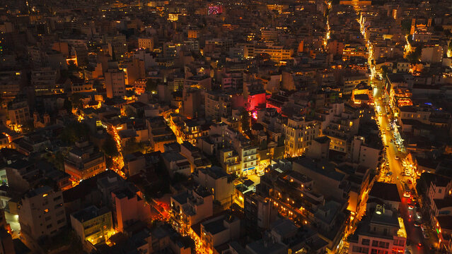 Aerial view of the illuminated urban landscape of Athens at night, featuring dense residential buildings, glowing street lights, and narrow roads in Greece.