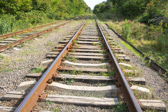 Parallel railway tracks with wooden and concrete sleepers stretching into a green wooded corridor