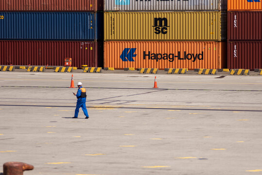 Dock worker walking along the quay beside rows of stacked shipping containers at a busy commercial container terminal.