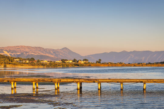Seaside landscape near the city of Vlore in Albania, Europe. A serene landscape featuring a wooden pier extending over calm lake water with distant mountains under a clear blue sky