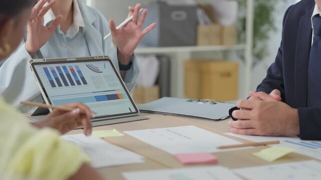 Business professionals point at data trends on a tablet screen capturing detailed market analysis hands analyzing stock market charts on a tablet, colleagues gathered around during a financial review 