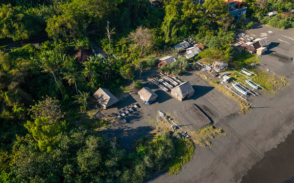 Aerial view of the natural salt maker in Kusamba with traditional thatched-roof huts, wooden evaporation trays, and small outrigger boats on the black sand beach in Kecamatan Dawan, Bali, Indonesia.