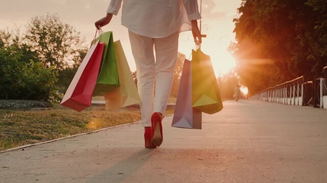 Woman walking with colorful shopping bags at sunset, dynamic footage of successful retail therapy.