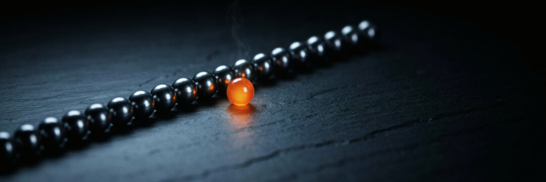 Single glowing orange bead breaking a diagonal row of dark glossy beads on a black surface, weak point in the line, concept