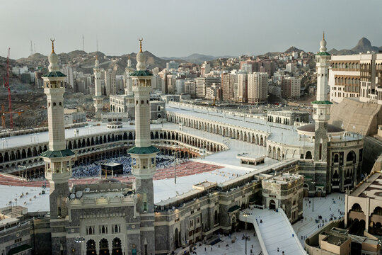 Aerial view of Masjid al-Haram with its towering minarets and the Kaaba, surrounded by the expansive white marble courtyard and urban architecture of Makkah, Makkah Province, Saudi Arabia.