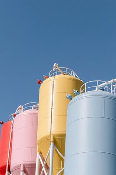 Pastel-colored industrial storage silos photographed from a low angle against a clear blue sky