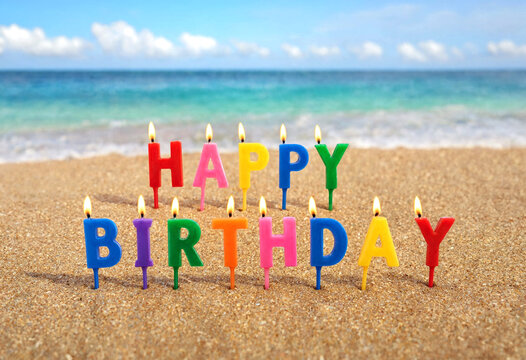 Colorful birthday candles spelling happy birthday on sandy beach