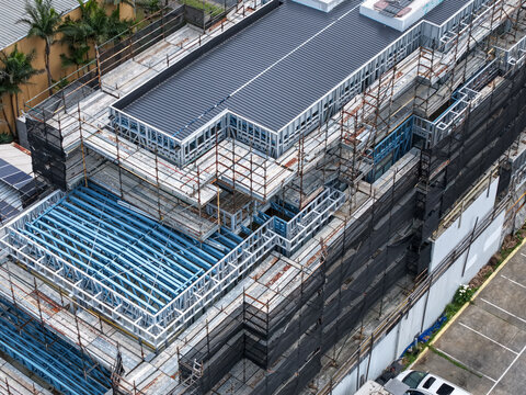 Aerial view of a building under construction featuring steel framing and extensive scaffolding covered in black safety netting in Melbourne, VIC, Australia.
