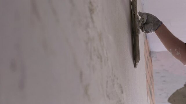 Worker applying plaster to wall with trowel during interior finishing