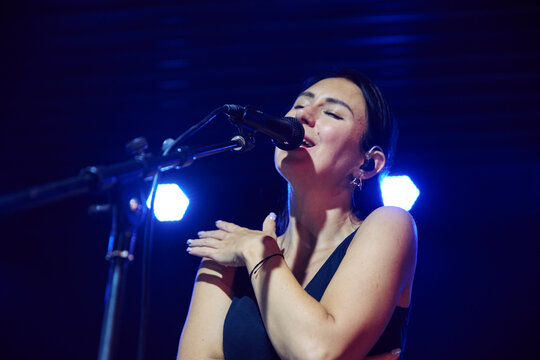 Young woman singing into microphone during concert sound check under blue light