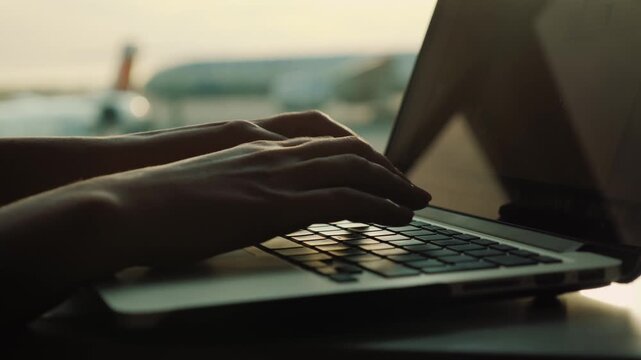 Person typing on laptop computer near airplane at airport window cinematic footage.