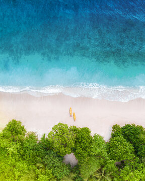 Aerial view of Pantai Gatra with two yellow kayaks resting on the white sand beach, bordered by lush green trees and turquoise ocean waves in Malang Regency, East Java, Indonesia.