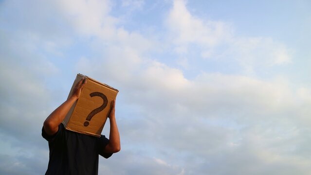 Person with Cardboard Box over Head and Question Mark Symbol Against Cloudy Sky.