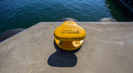 Yellow ten ton mooring bollard beside harbor water. © Trygve